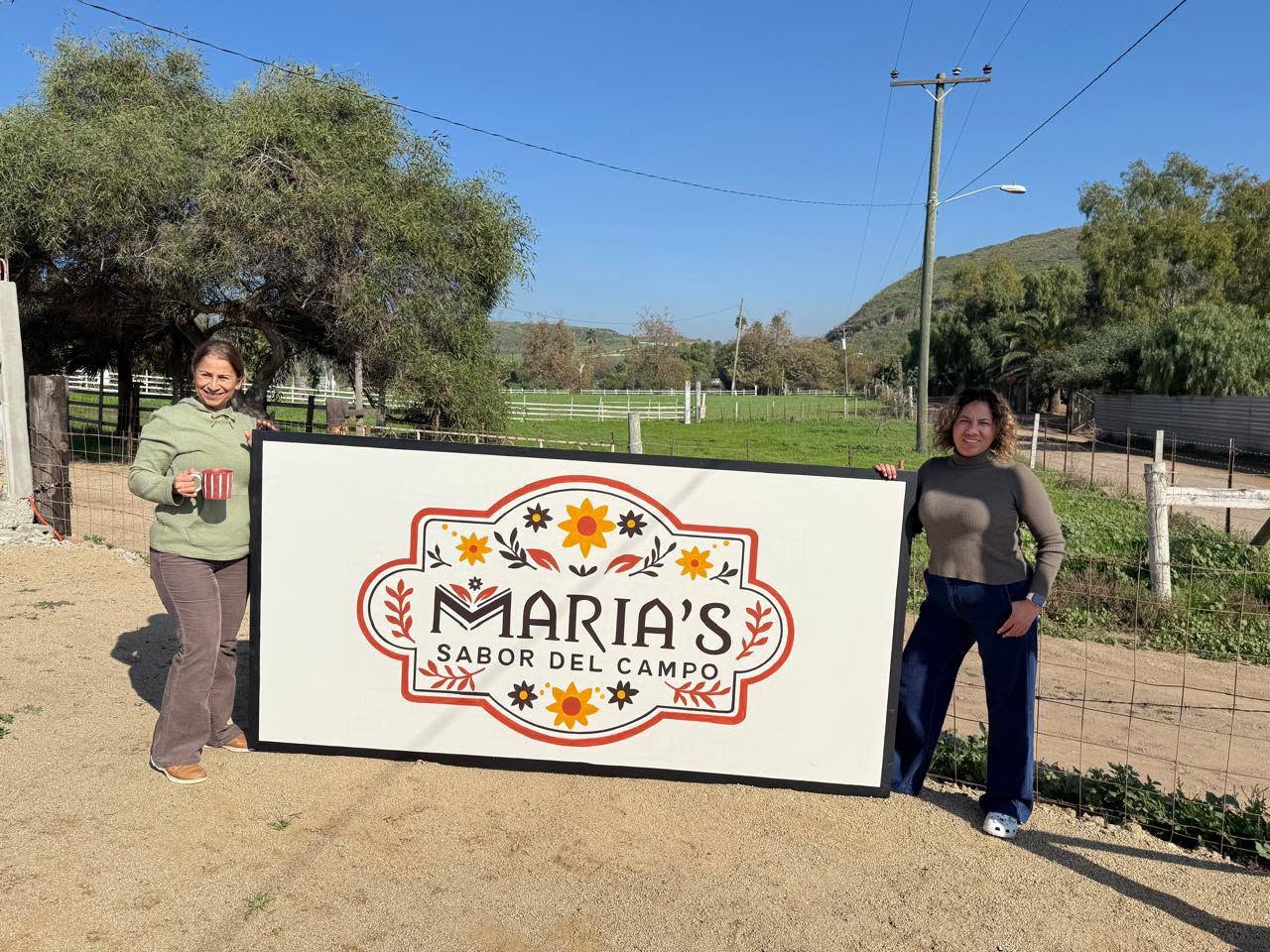 Las dueñas de María's Sabor del Campo junto al letrero del rancho