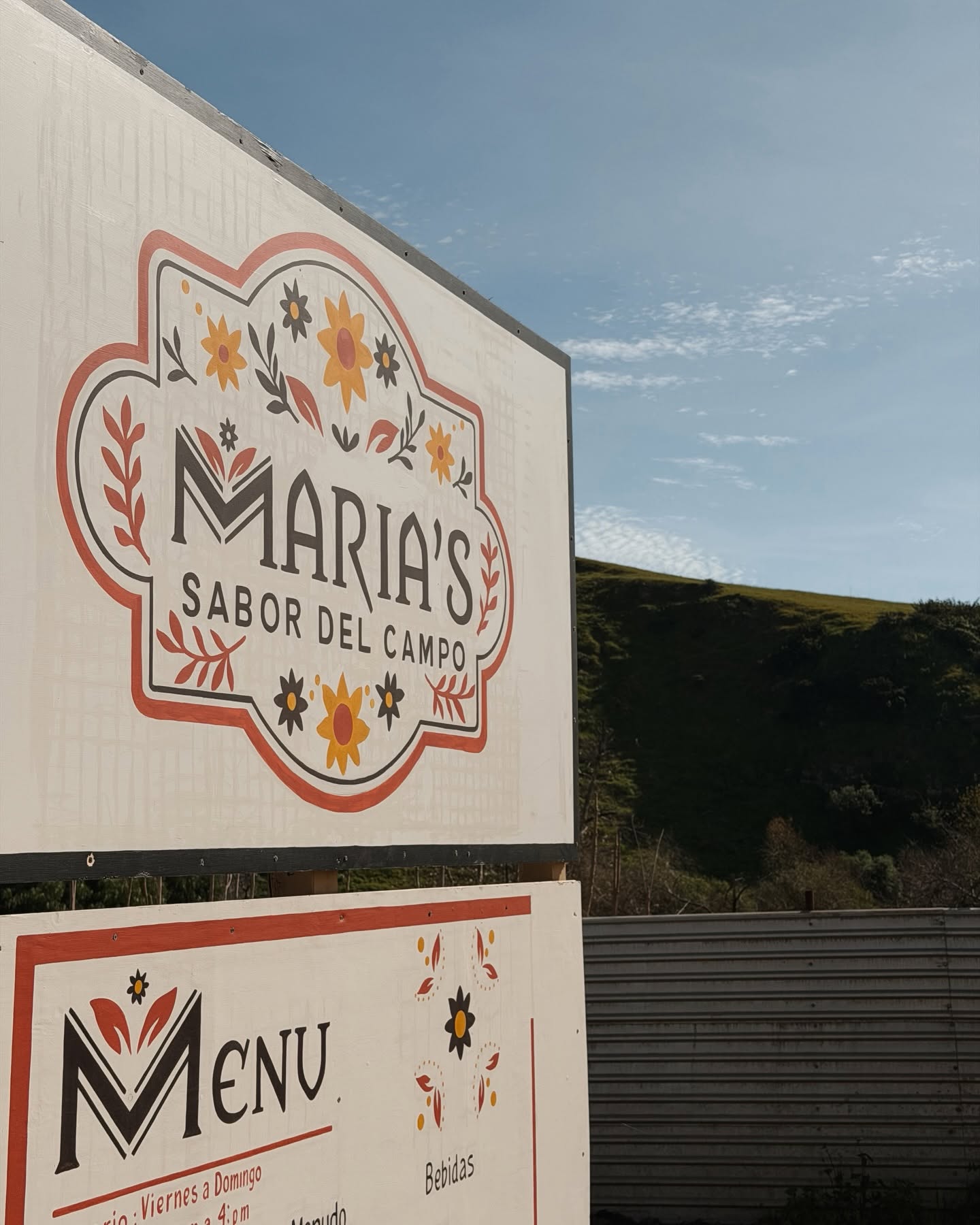 Letrero pintado a mano de María's Sabor del Campo junto al cerro
